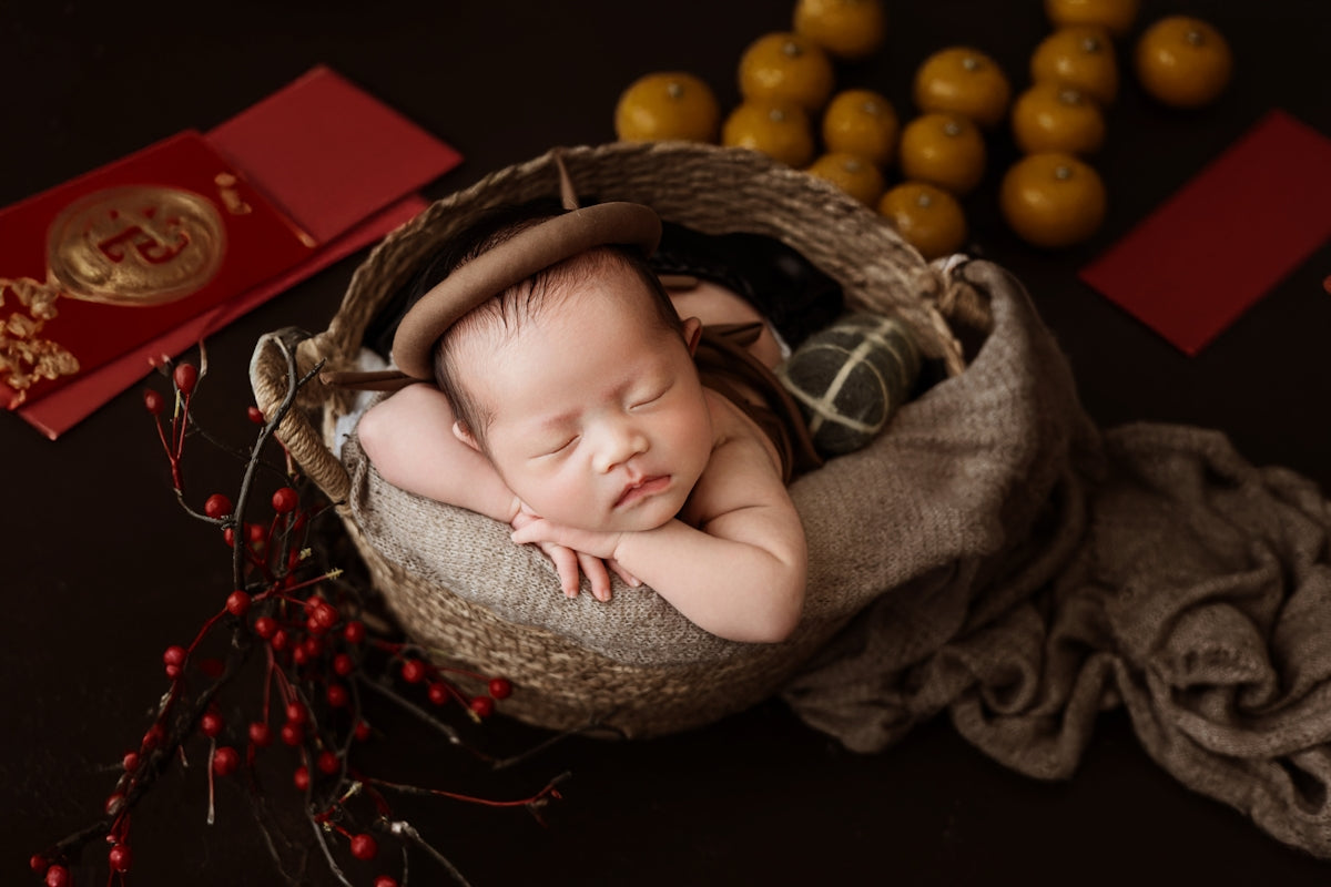 A baby sleeping in a basket next to some oranges