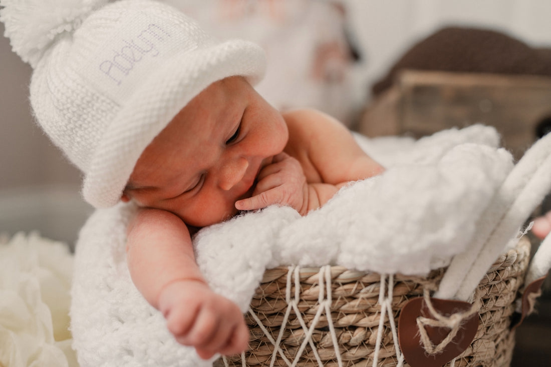 Newborn baby sleeping in a basket with a white hat.