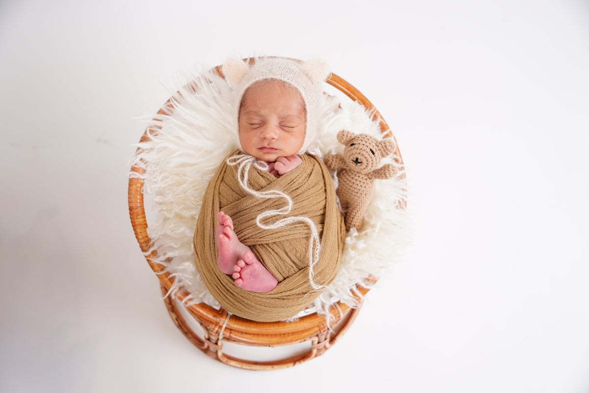 Newborn baby wrapped in blanket with teddy bear.